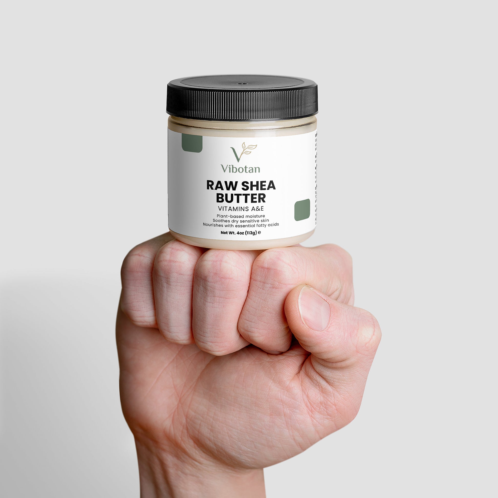 Hand holding a jar of NaturaVital Raw Shea Butter against a light gray background