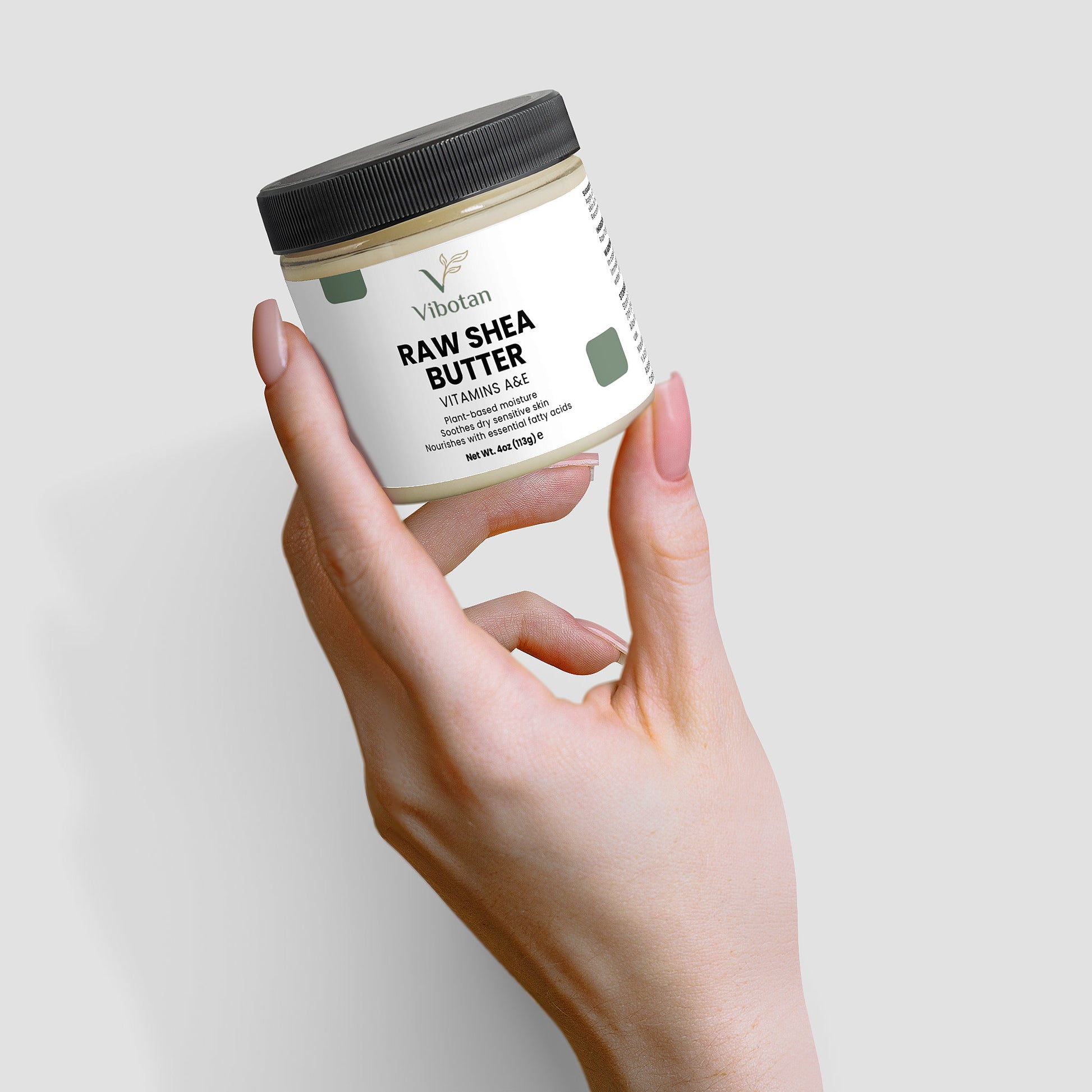 Hand holding a jar of Raw Shea Butter against a light gray background